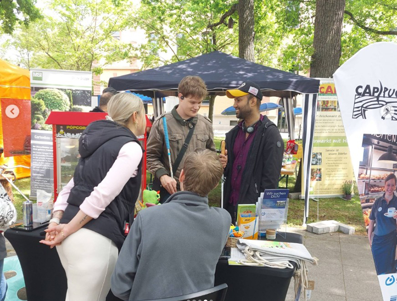 Teilnehmende im Gespräch an einem Messestand Teilnehmende im Gespräch an einem Messestand